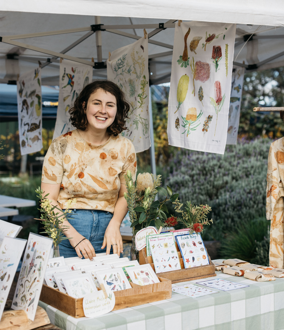 brunette woman standing at a market stall with art 