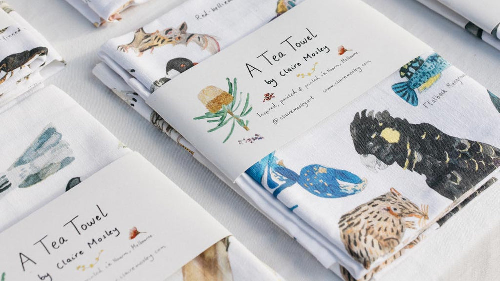 A close up photo of a market stall display featuring illustrated linen tea towels