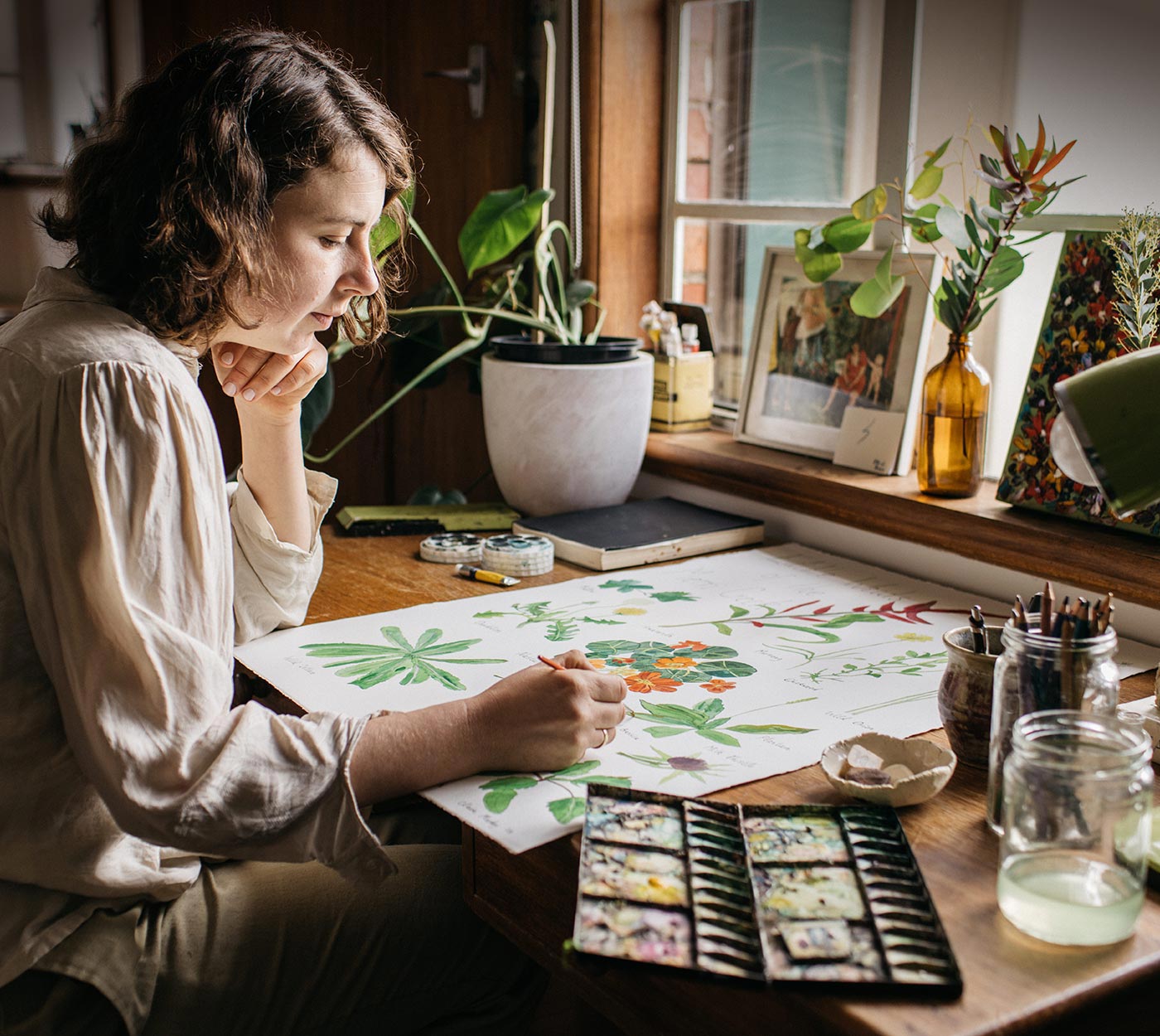 Brunette woman sitting at desk painting flowers with watercolour paints